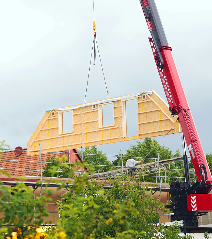 assembly of a prefabricated timber house, crane lifting a gable component in the air