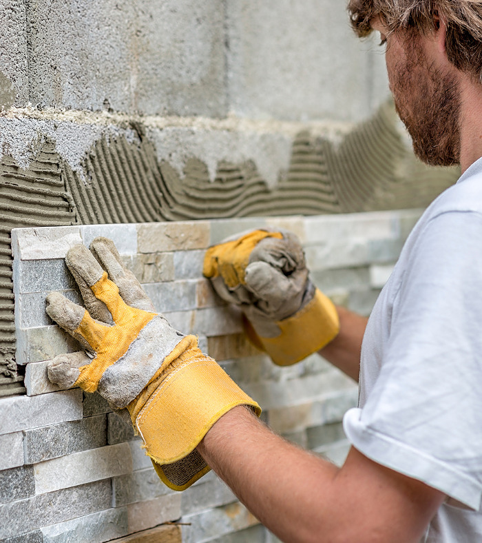 Man pressing an ornamental tile into a glue on a wall with gloved hands in a DIY concept.