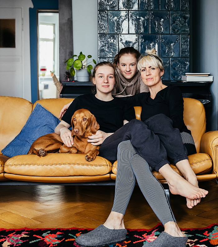 A family portrait of a single mom sitting with on a leather sofa with her two daughters and the family dog in their living room at home together.