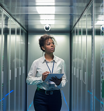 African American woman using tablet while walking in corridor of data center and checking hardware on server racks