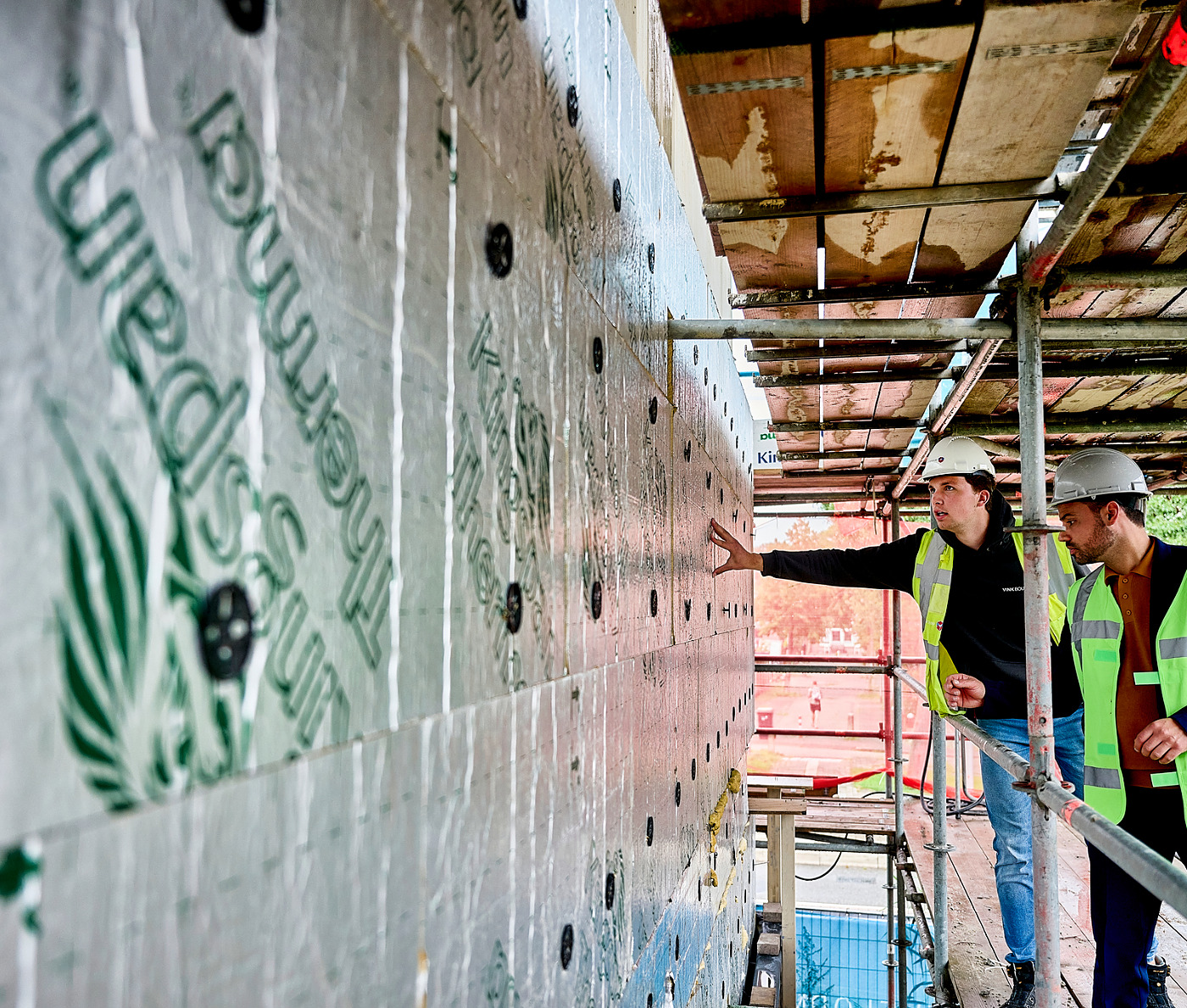 Aannemer en bouwvakkers lopen over de bouwplaats van een nieuw bedrijfspand en bekijken en bespreken de isolatie